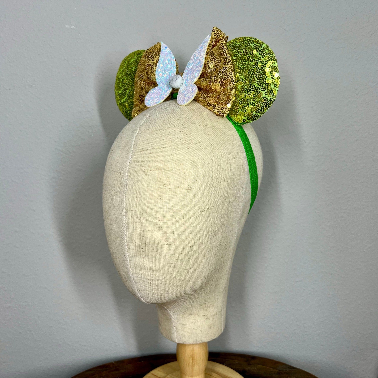 Green sequin mouse ears headband with gold bow and glitter fairy wings on a mannequin