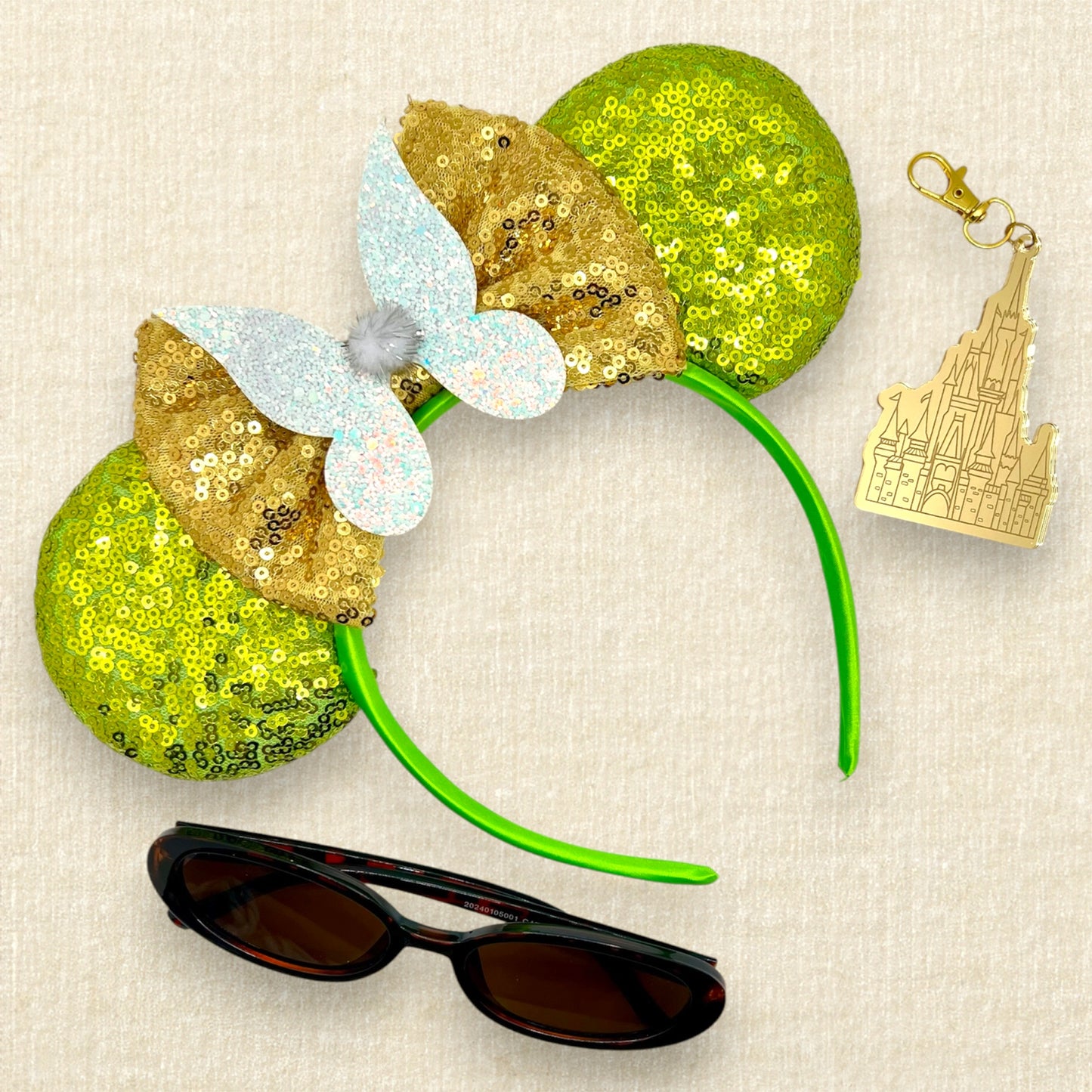Light green sequin mouse ears headband with gold bow, glitter fairy wings, and pom-pom centerpiece; sunglasses; castle keychain