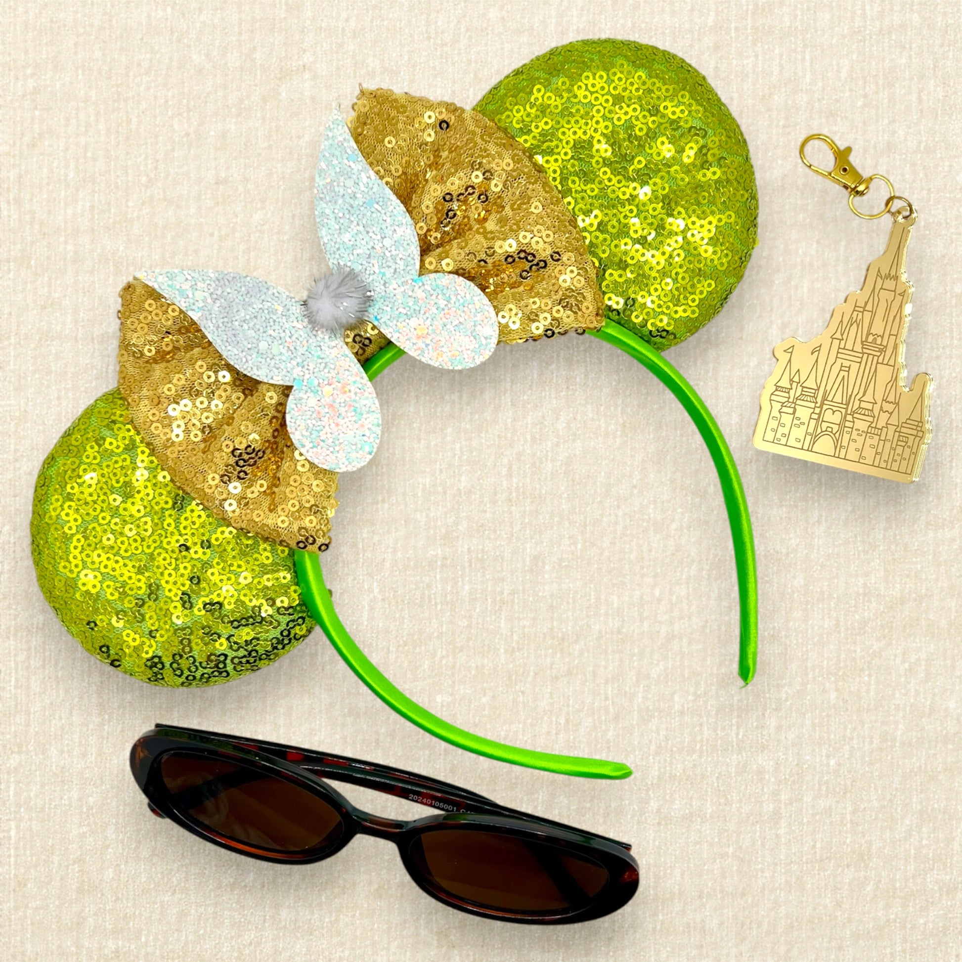 Light green sequin mouse ears headband with gold bow, glitter fairy wings, and pom-pom centerpiece; sunglasses; castle keychain