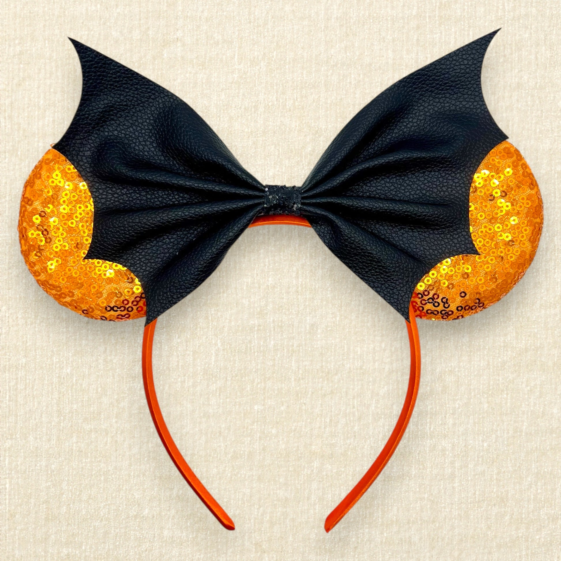 Halloween-themed mouse ears headband with orange sequin ears and black faux leather bat wing bow