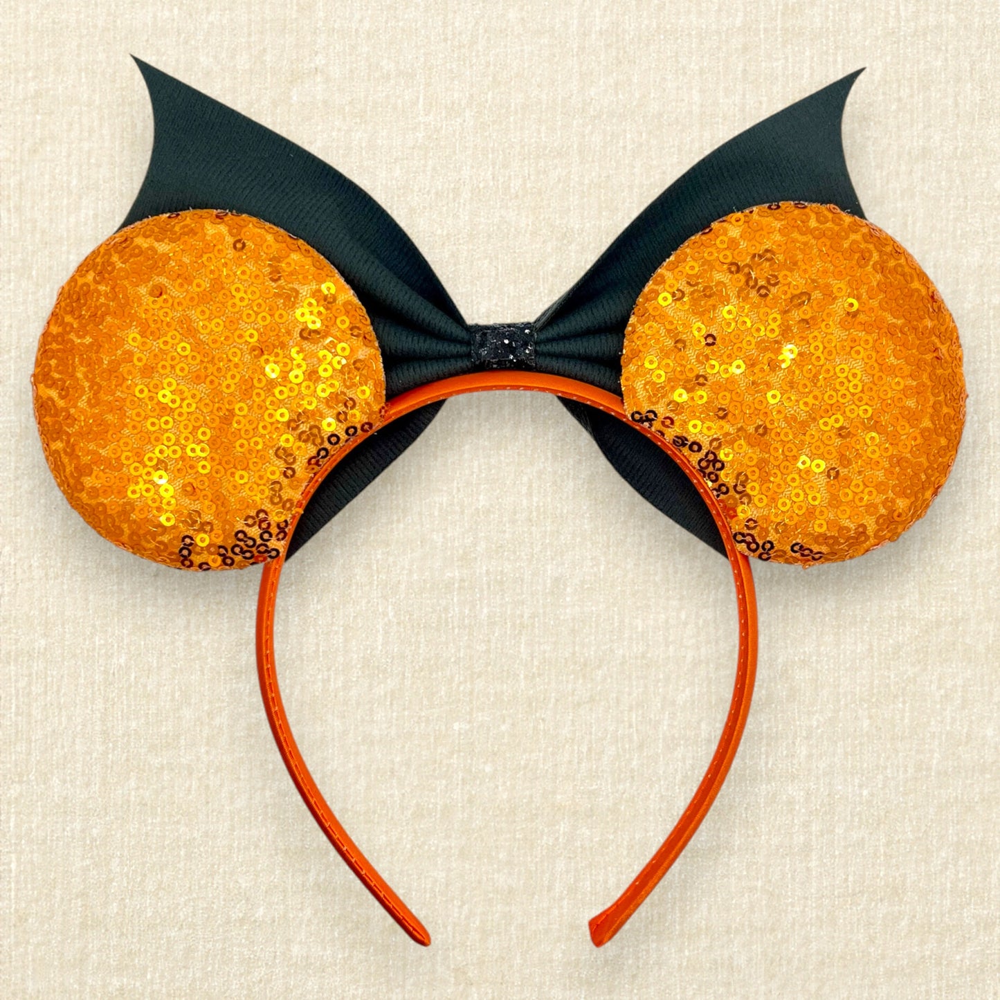 Halloween-themed mouse ears headband with orange sequin ears and black faux leather bat wing bow (back view)