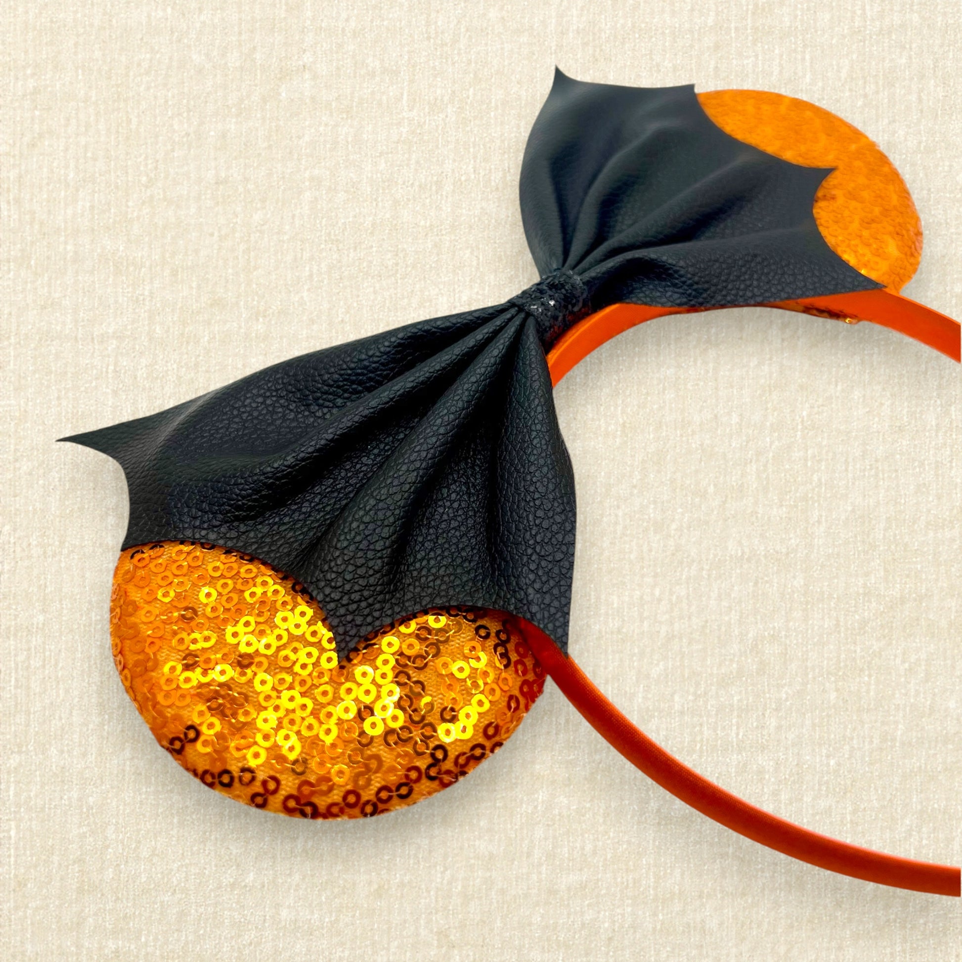 Halloween-themed mouse ears headband with orange sequin ears and black faux leather bat wing bow