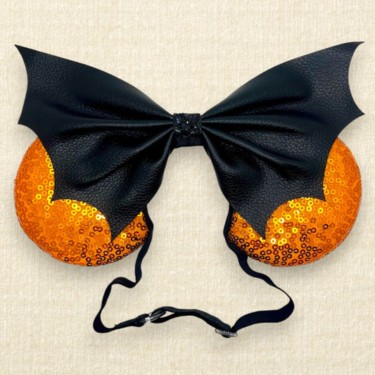 Halloween-themed mouse ears with orange sequin ears and black faux leather bat wing bow on an elastic headband