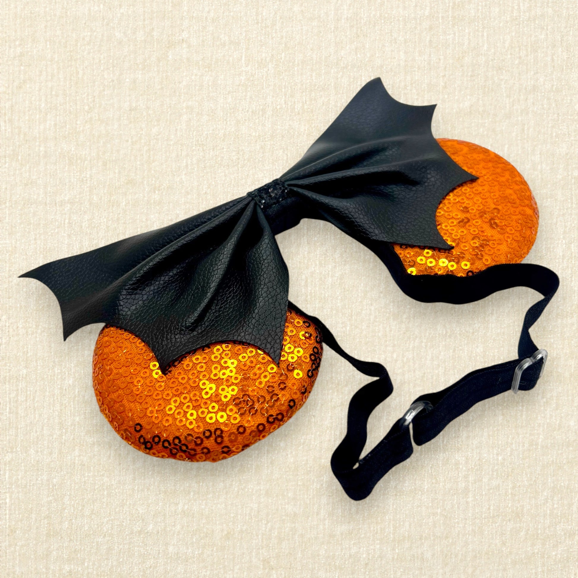 Halloween-themed mouse ears with orange sequin ears and black faux leather bat wing bow on an elastic headband