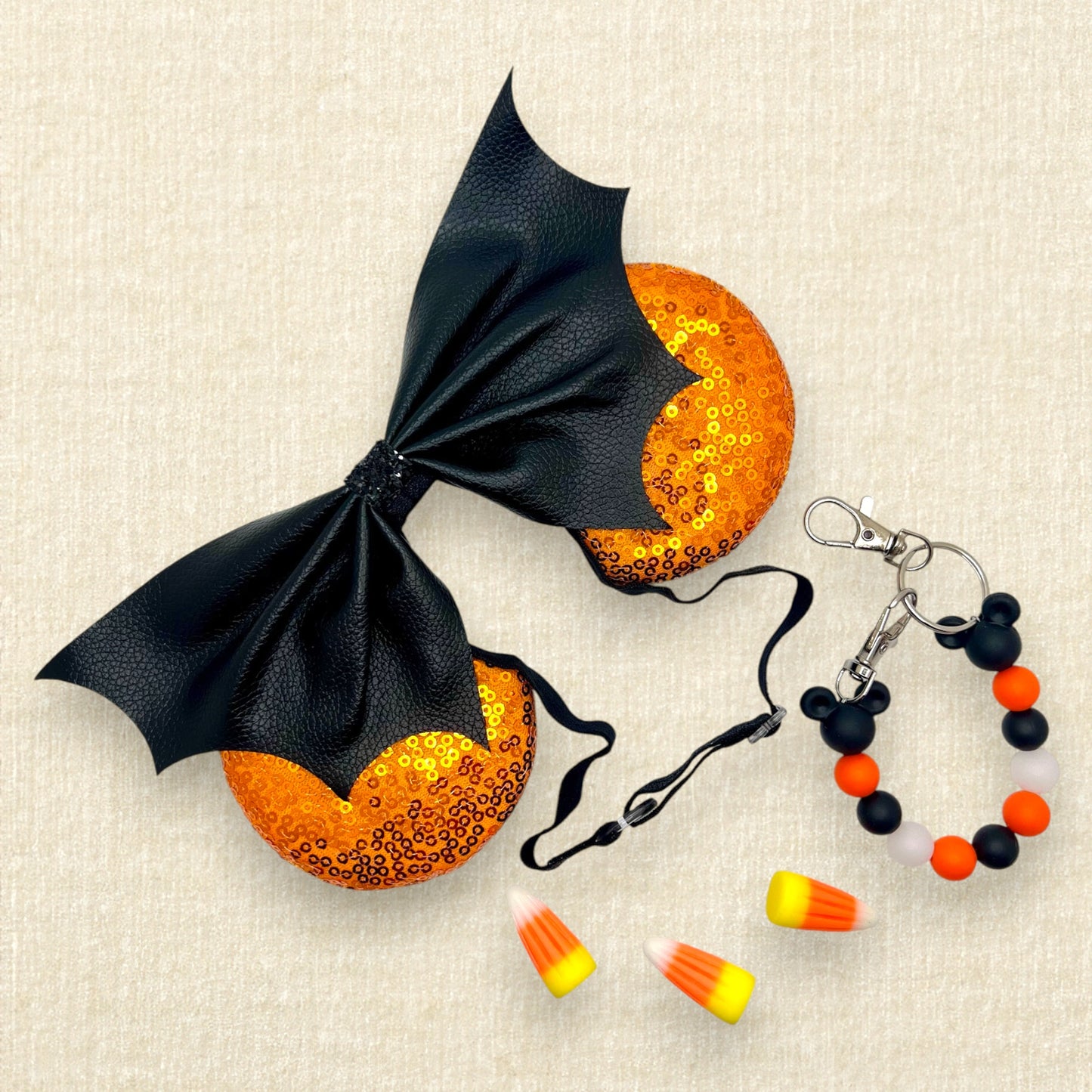 Halloween-themed mouse ears with orange sequin ears and black faux leather bat wing bow on an elastic headband; candy corn pieces; black and orange beaded mouse ears holder keychain
