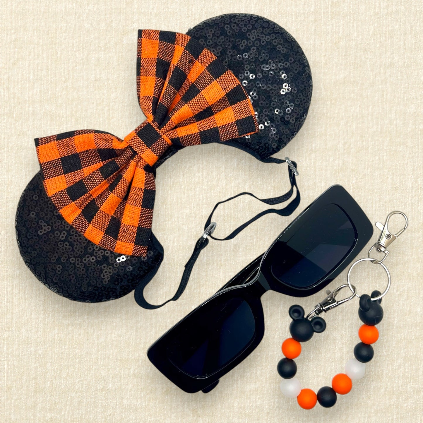 Fall-themed mouse ears with black ears and orange and black buffalo plaid bow on an elastic headband; black sunglasses; orange and black beaded mouse ears holder keychain