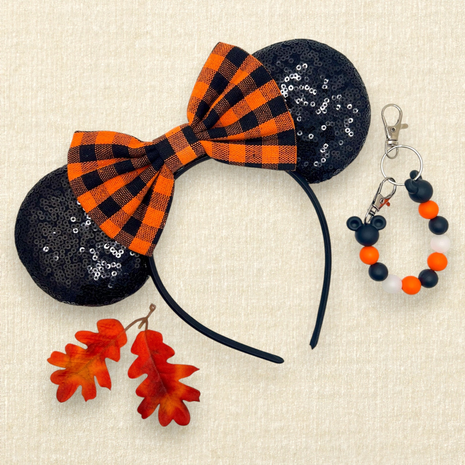 Fall-themed mouse ears with black sequin mouse ears and orange and black buffalo plaid bow; red and orange leaves; black and orange beaded mouse ears holder keychain