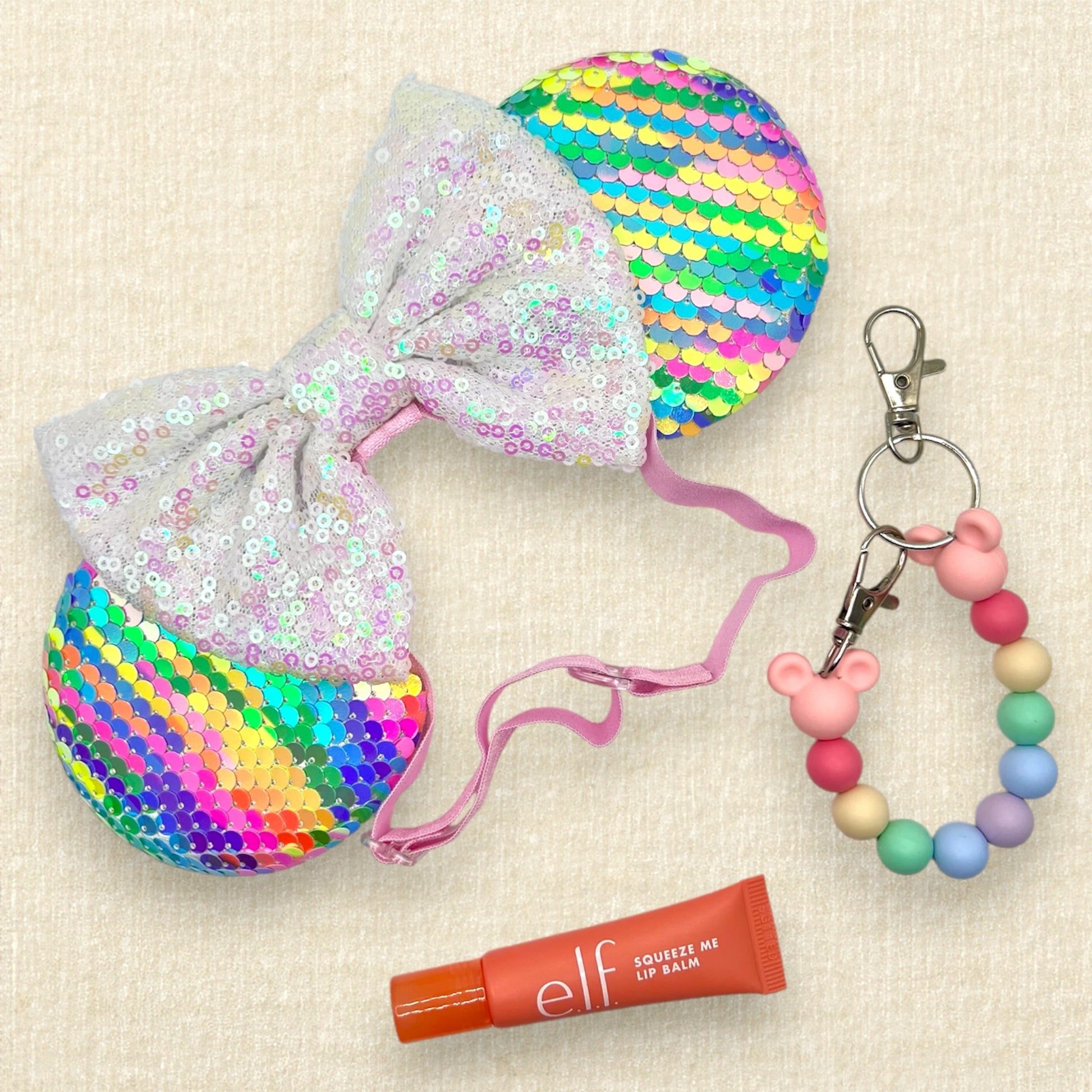 Colorful sequin mouse ears with white sequin bow on an elastic headband; pink lip balm; colorful beaded mouse ears holder clip