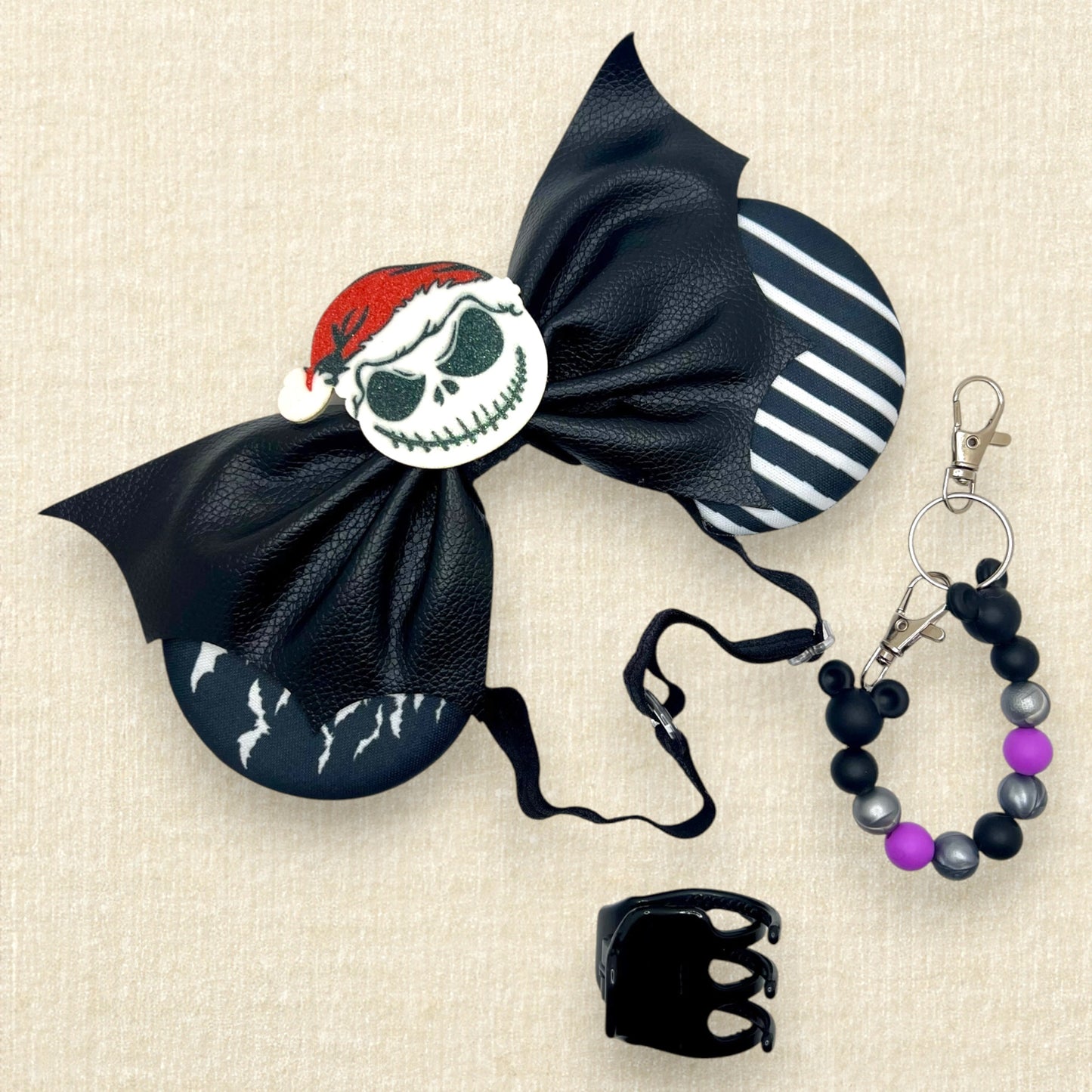 Halloween-themed mouse ears with black and white fabric ears, black faux leather bat wing bow, and glitter Sandy Claws centerpiece on an elastic headband; black claw clip; purple, black, and silver beaded mouse ears holder keychain