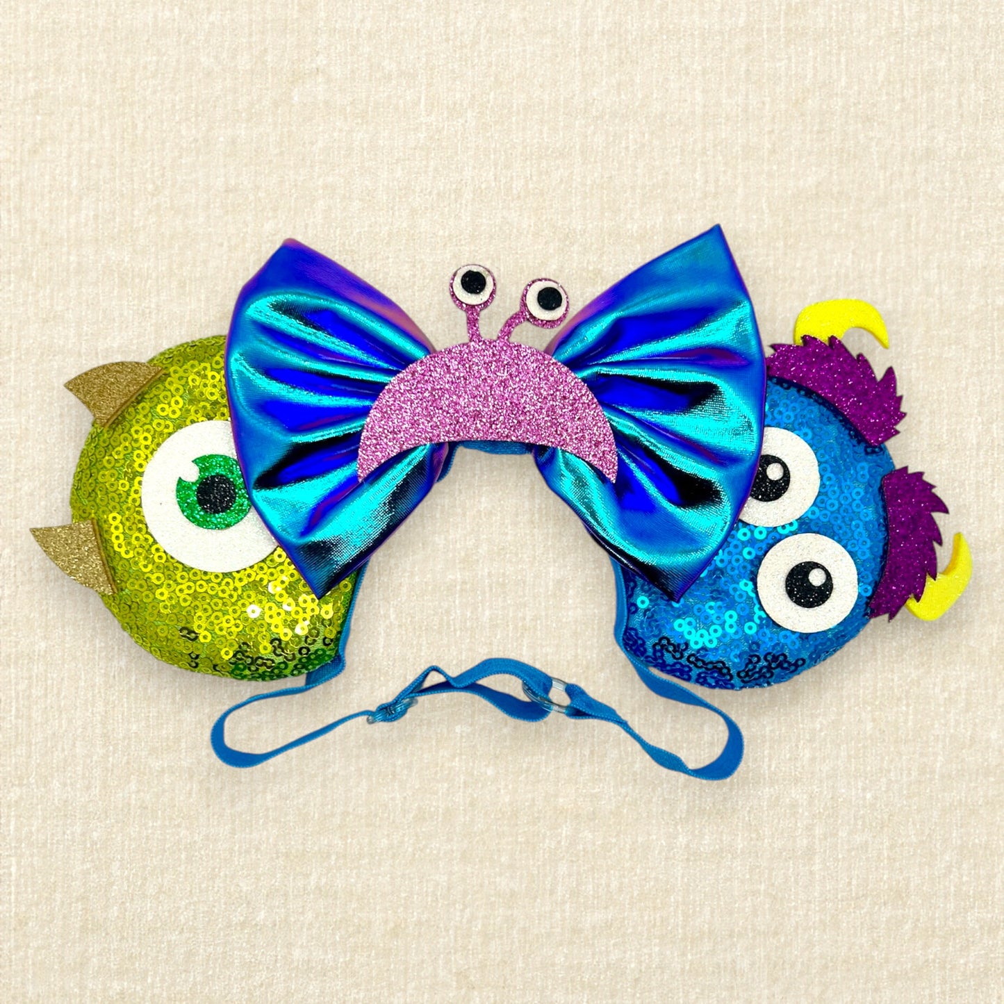 Green and blue sequin mouse ears with glitter monster details and an iridescent blue bow on an elastic headband 