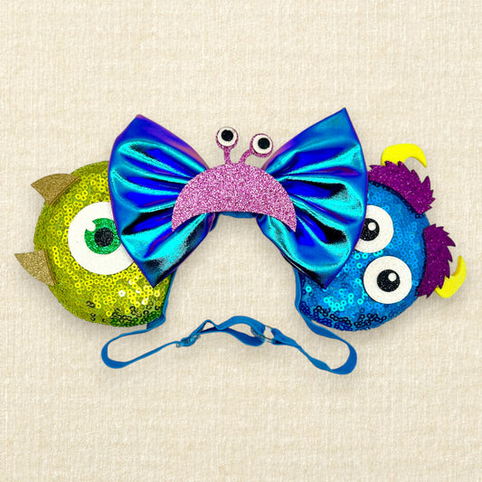 Green and blue sequin mouse ears with glitter monster details and an iridescent blue bow on an elastic headband 
