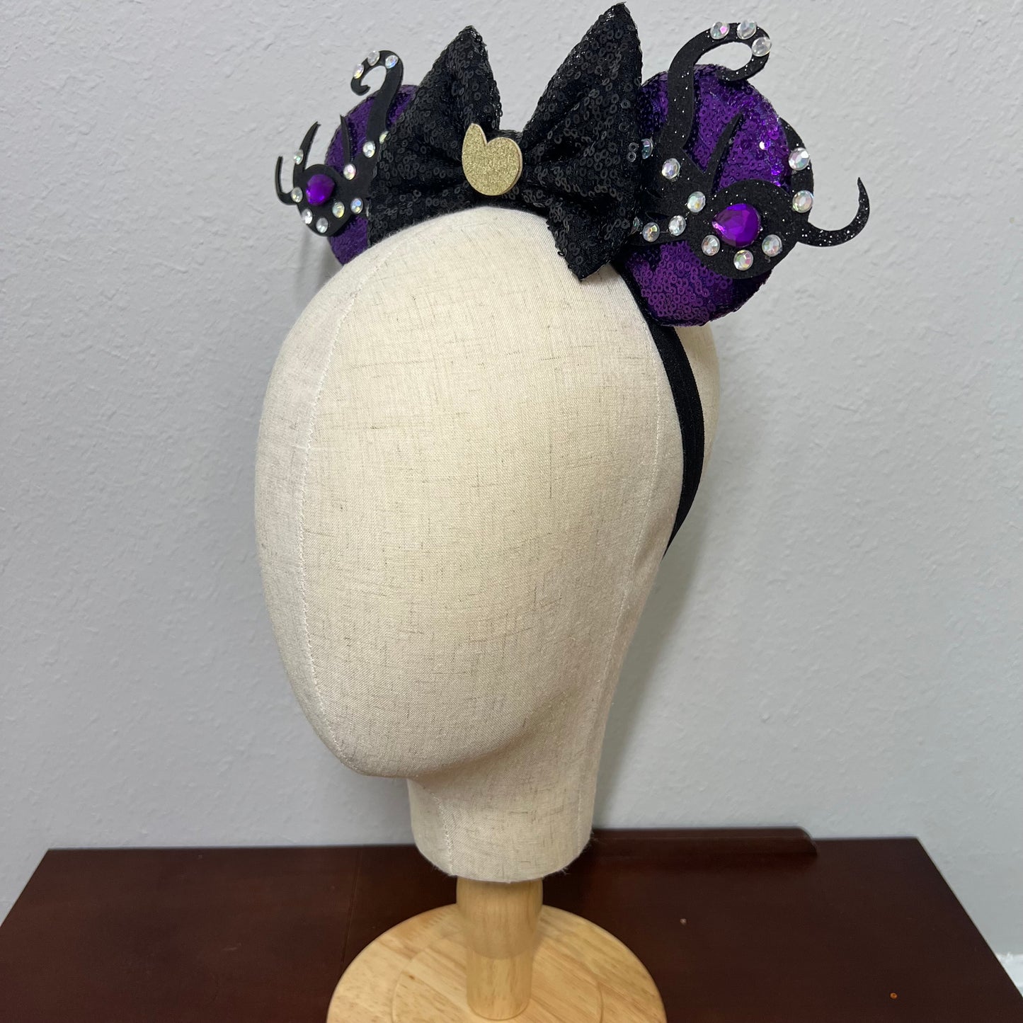 Black and purple mouse ears headband on a mannequin head against a plain background