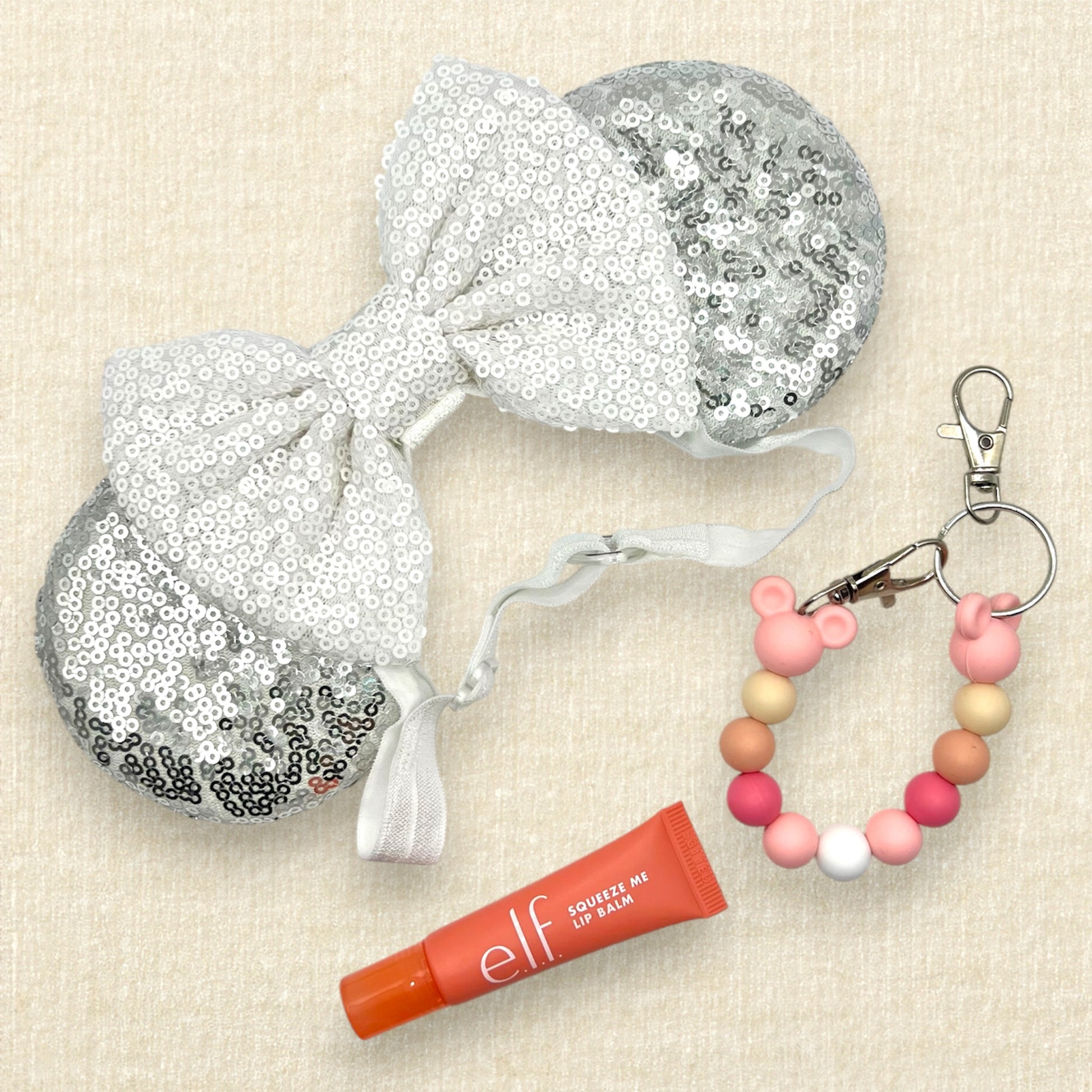 Silver mouse ears with white sequin bow on an elastic headband; pink lip balm; pink beaded mouse ears holder clip