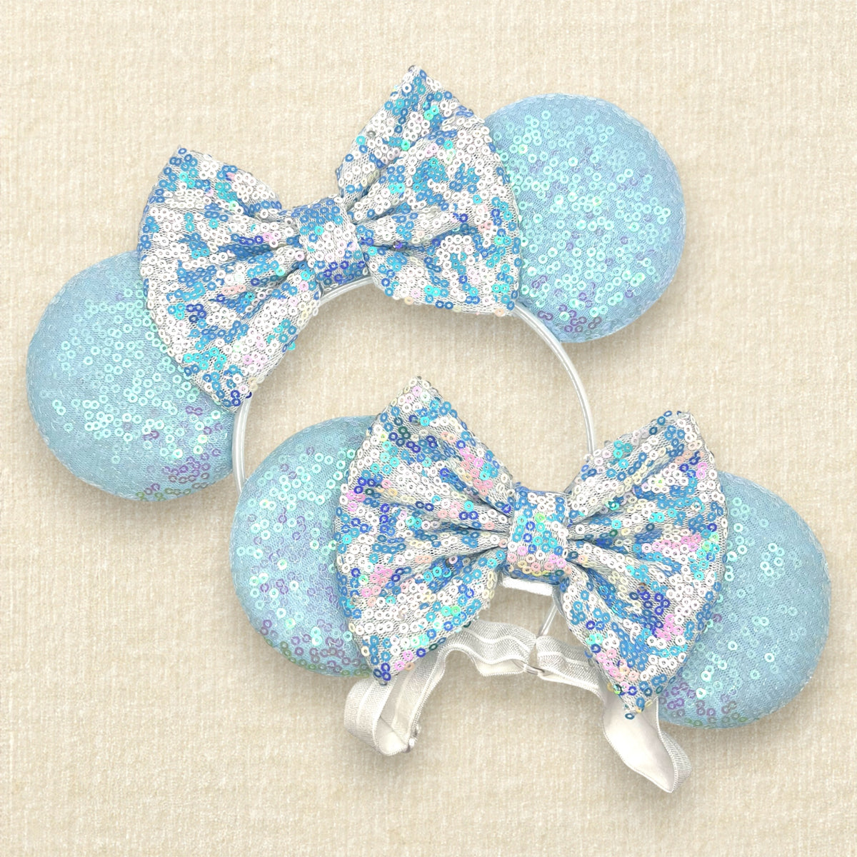 Matching winter mouse ears with iridescent light blue sequin mouse ears and a white and blue sequin bow, one with a standard headband and one with an elastic headband