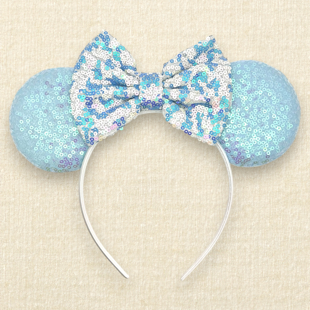 A winter-themed mouse ears headband with iridescent light blue sequin mouse ears and a blue and white sequin bow