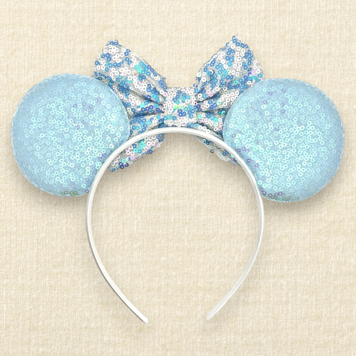 A winter-themed mouse ears headband with iridescent light blue sequin mouse ears and a blue and white sequin bow (back view)