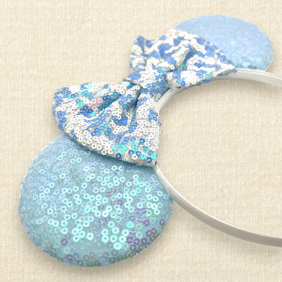 A winter-themed mouse ears headband with iridescent light blue sequin mouse ears and a blue and white sequin bow
