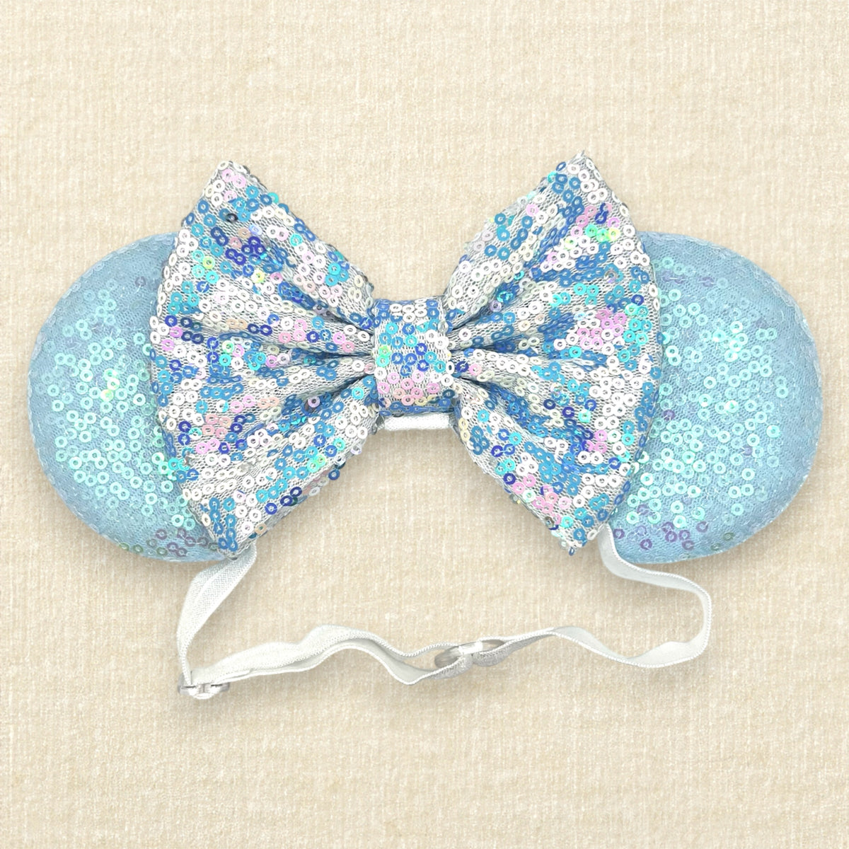 A winter-themed mouse ears headband with iridescent light blue sequin mouse ears and a blue and white sequin bow on an elastic headband