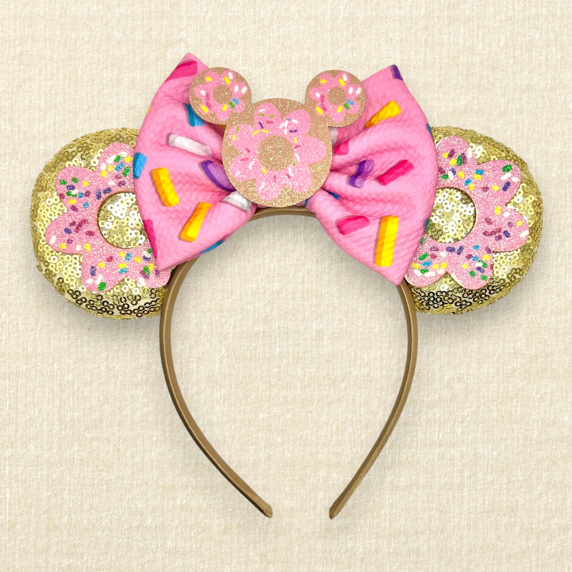 Gold mouse ears with pink glitter sprinkle donuts, a pink fabric bow with rainbow sprinkles, and a mouse-shaped donut centerpiece