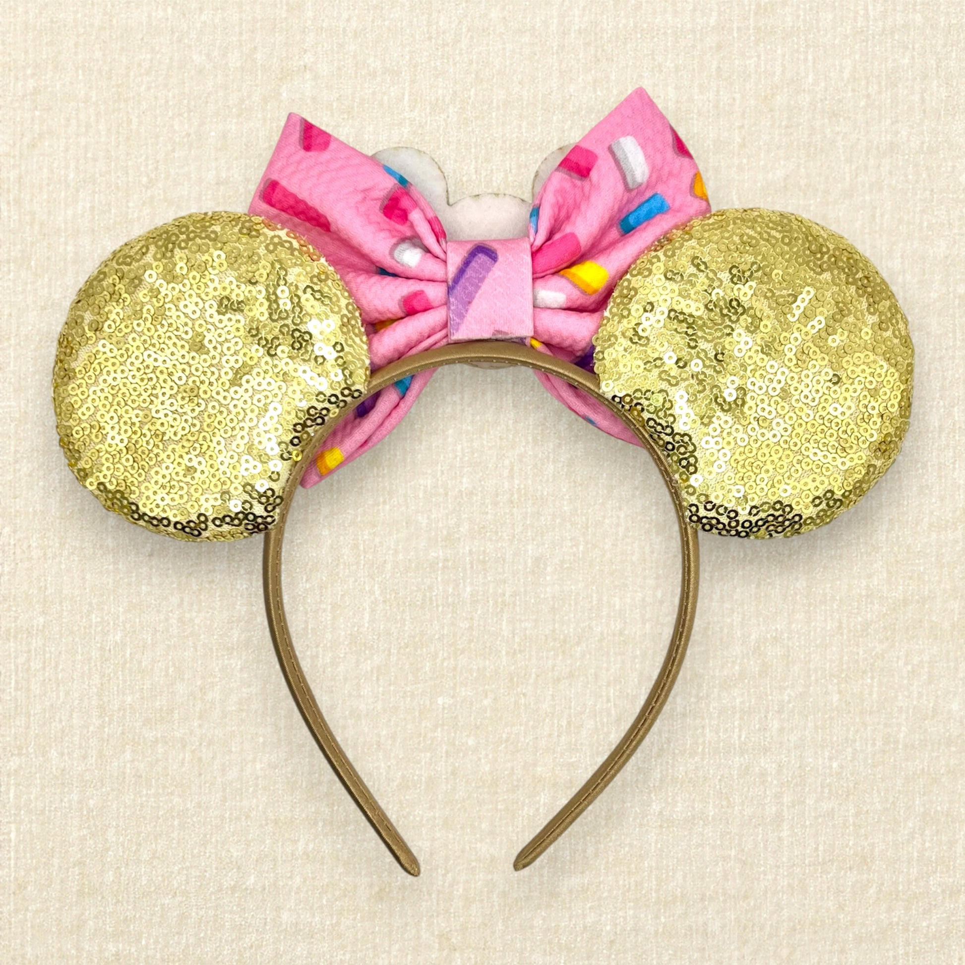 Gold mouse ears with pink glitter sprinkle donuts, a pink fabric bow with rainbow sprinkles, and a mouse-shaped donut centerpiece (back view)