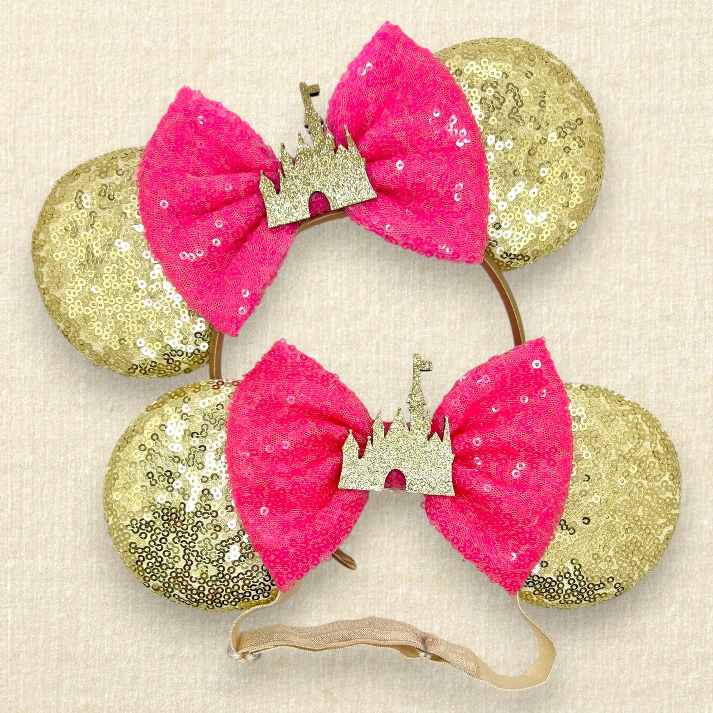 Pair of gold sequin mouse ears with hot pink bow and gold glitter castle, one with a standard headband and one with an elastic headband