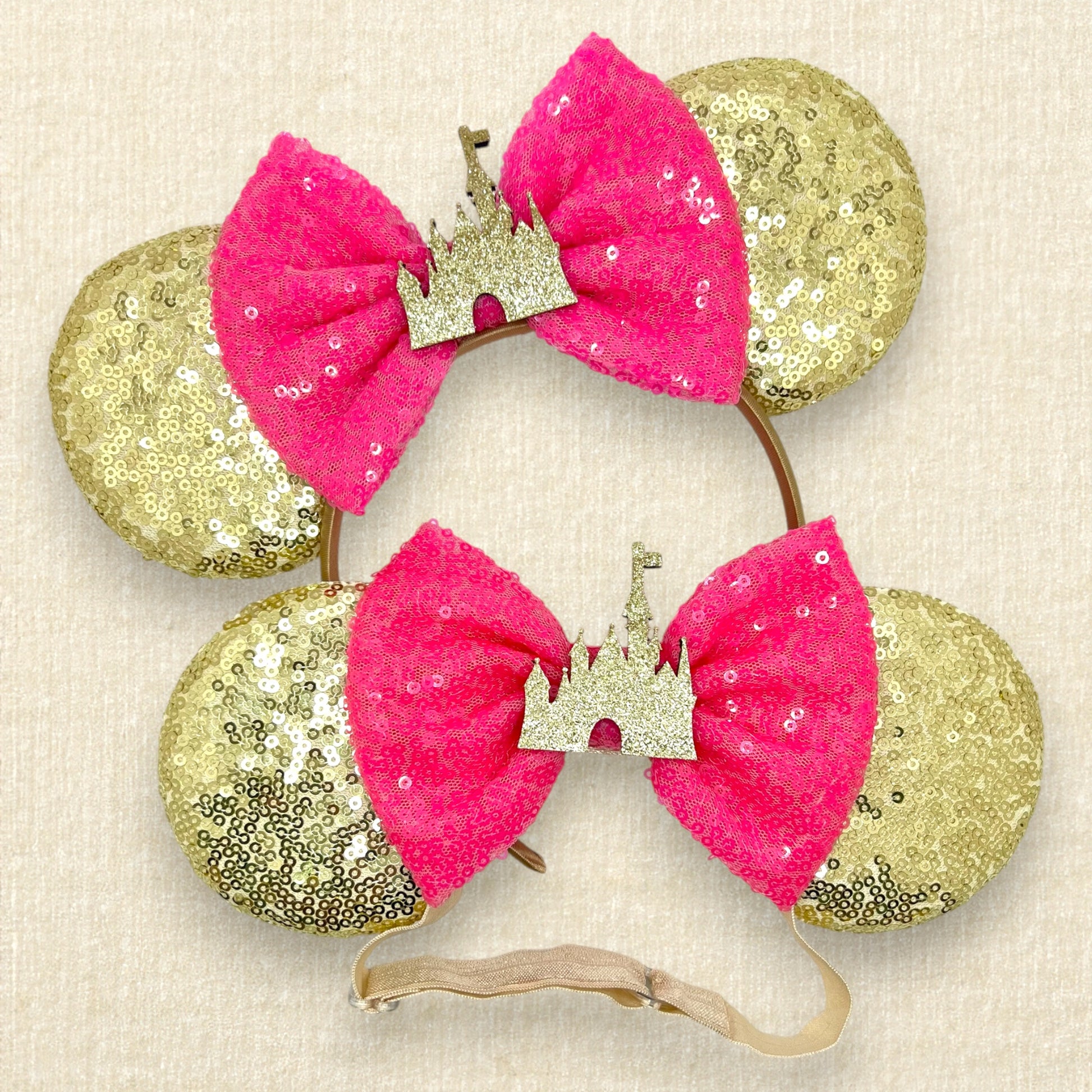 Pair of gold sequin mouse ears with hot pink bow and gold glitter castle, one with a standard headband and one with an elastic headband