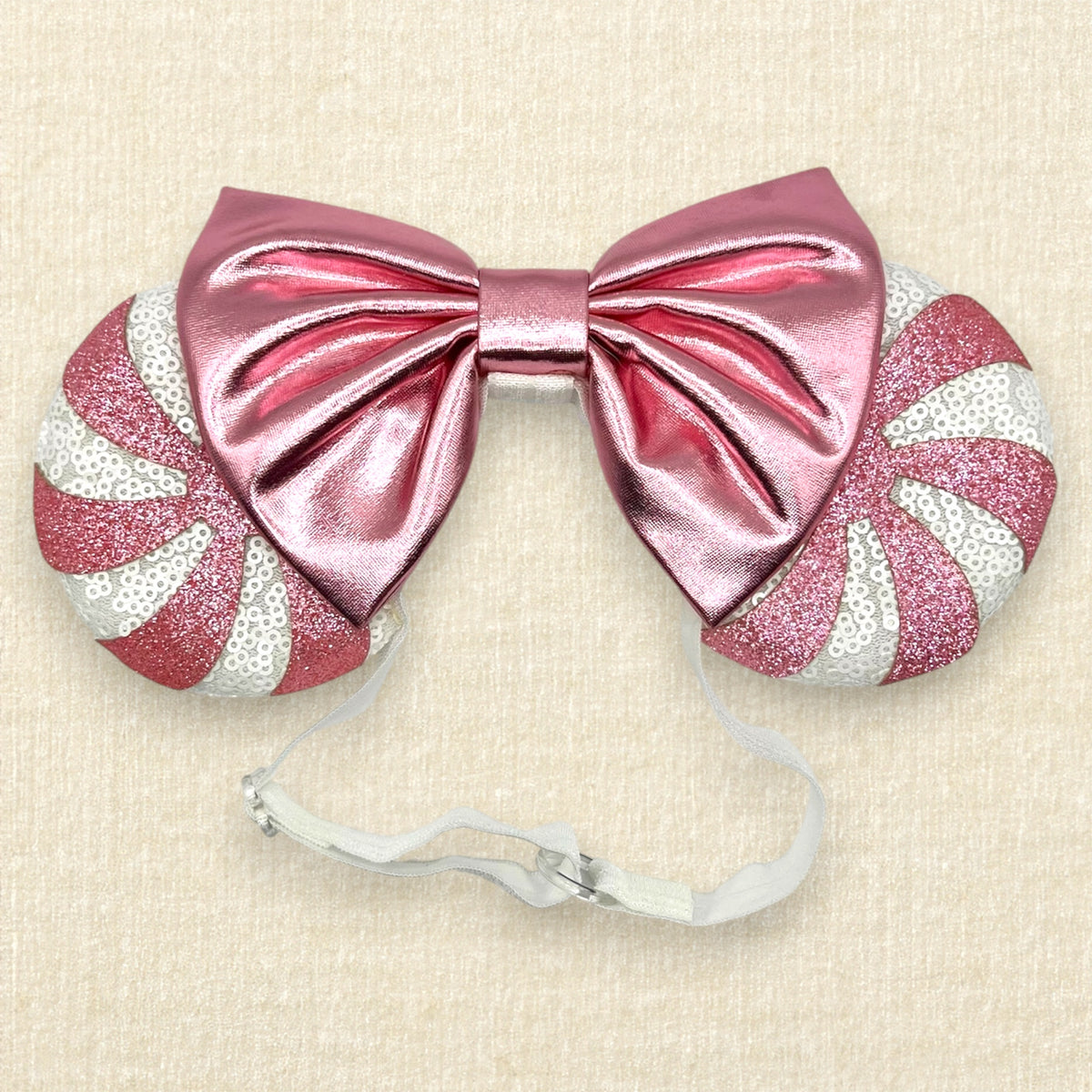 A festive pair of Christmas peppermint mouse ears with white sequin ears, pink glitter candy cane swirls, and a metallic pink bow on an elastic headband.