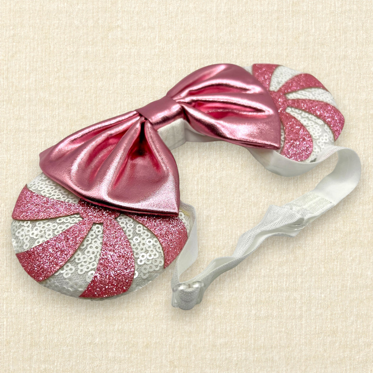 A festive pair of Christmas peppermint mouse ears with white sequin ears, pink glitter candy cane swirls, and a metallic pink bow on an elastic headband