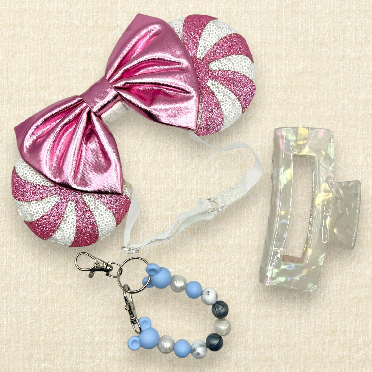A festive pair of Christmas peppermint mouse ears with white sequin ears, pink glitter candy cane swirls, and a metallic pink bow on an elastic headband; blue, pearl white, and silver beaded mouse ears holder keychain clip; and a pearl white claw clip