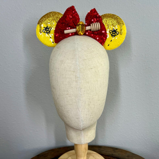 Decorative red and yellow mouse ears headband with red sequin bow, yellow ears, and honeycomb design on a mannequin.