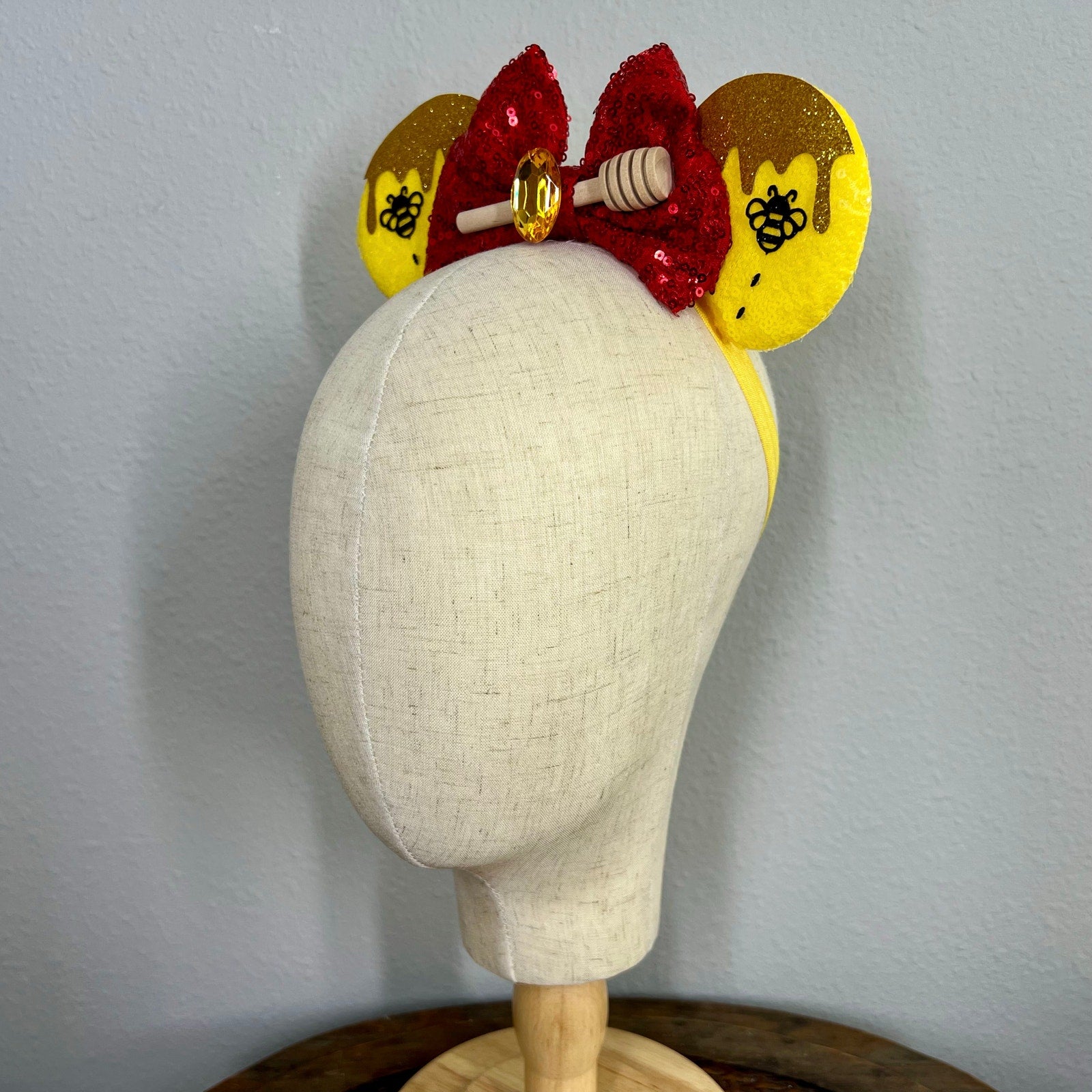 Decorative red and yellow mouse ears headband with red sequin bow, yellow ears, and honeycomb design on a mannequin.