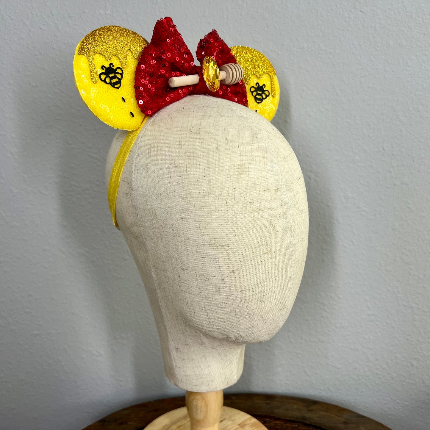 Decorative red and yellow mouse ears headband with red sequin bow, yellow ears, and honeycomb design on a mannequin.