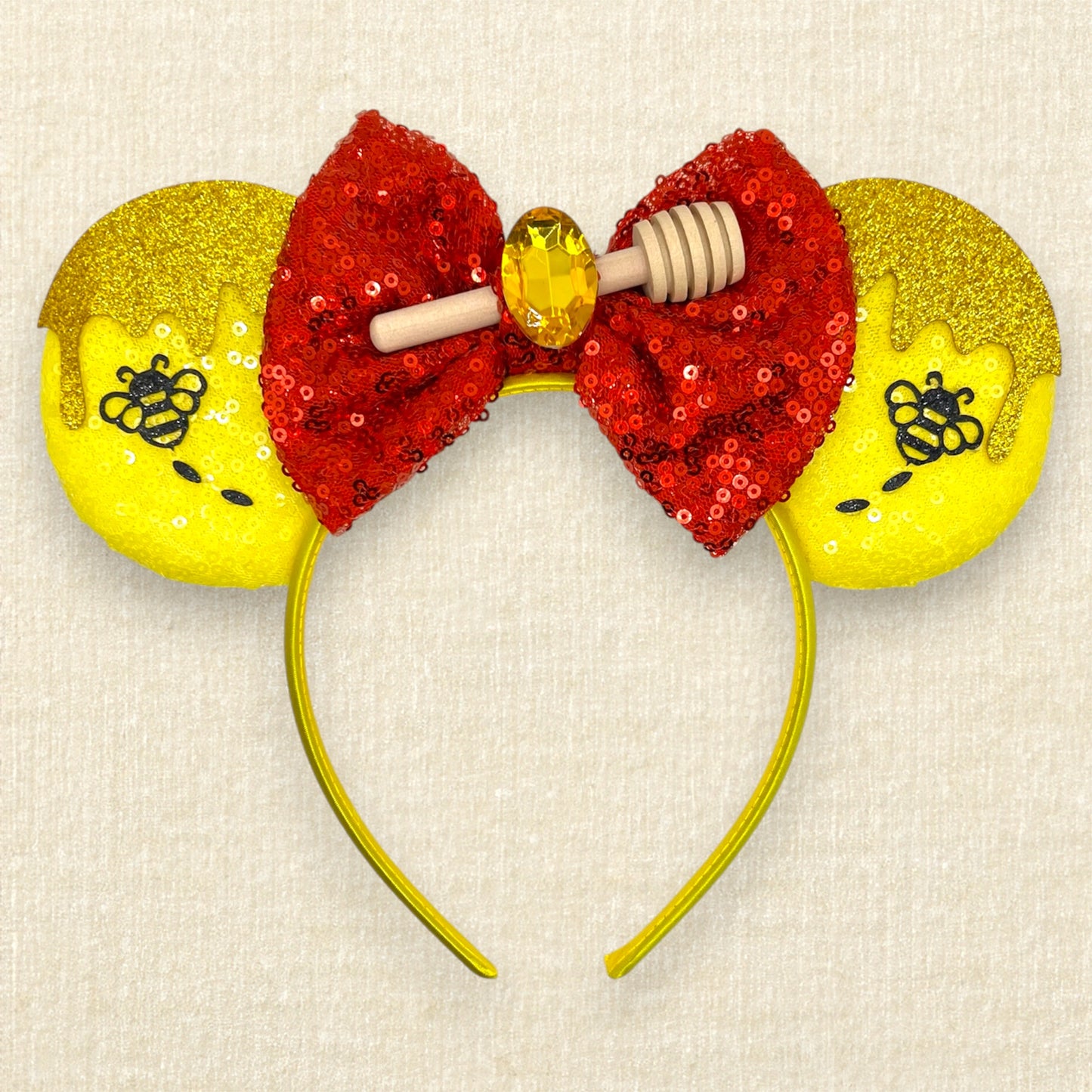 Yellow sequin mouse ears with gold glitter honey and black bumblebee accents, and red sequin bow with wooden honey dipper and gold rhinestone