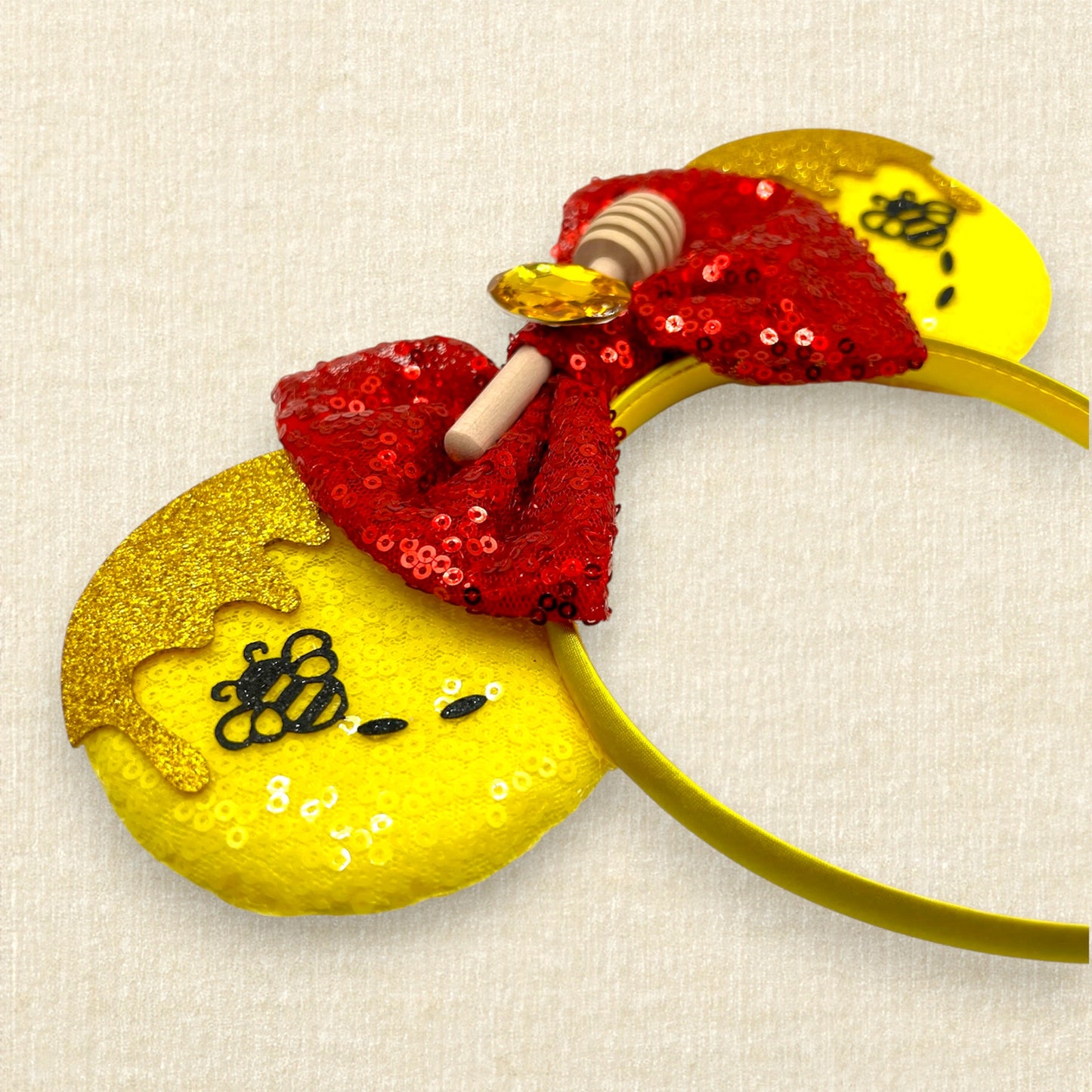 Yellow sequin mouse ears with gold glitter honey and black bumblebee accents, and red sequin bow with wooden honey dipper and gold rhinestone