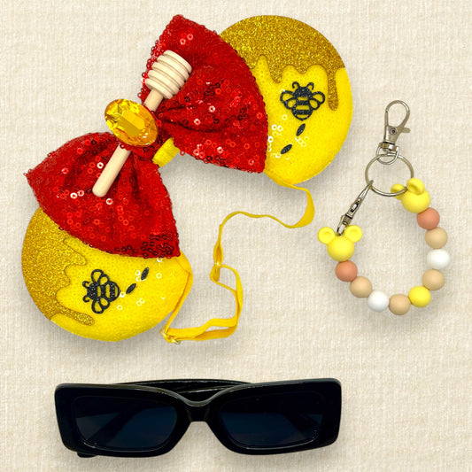 Yellow sequin mouse ears with glitter honey and bee accents, red sequin bow, wooden honey dipper, and yellow rhinestone on an elastic headband; black sunglasses; yellow beaded mouse ears holder keychain