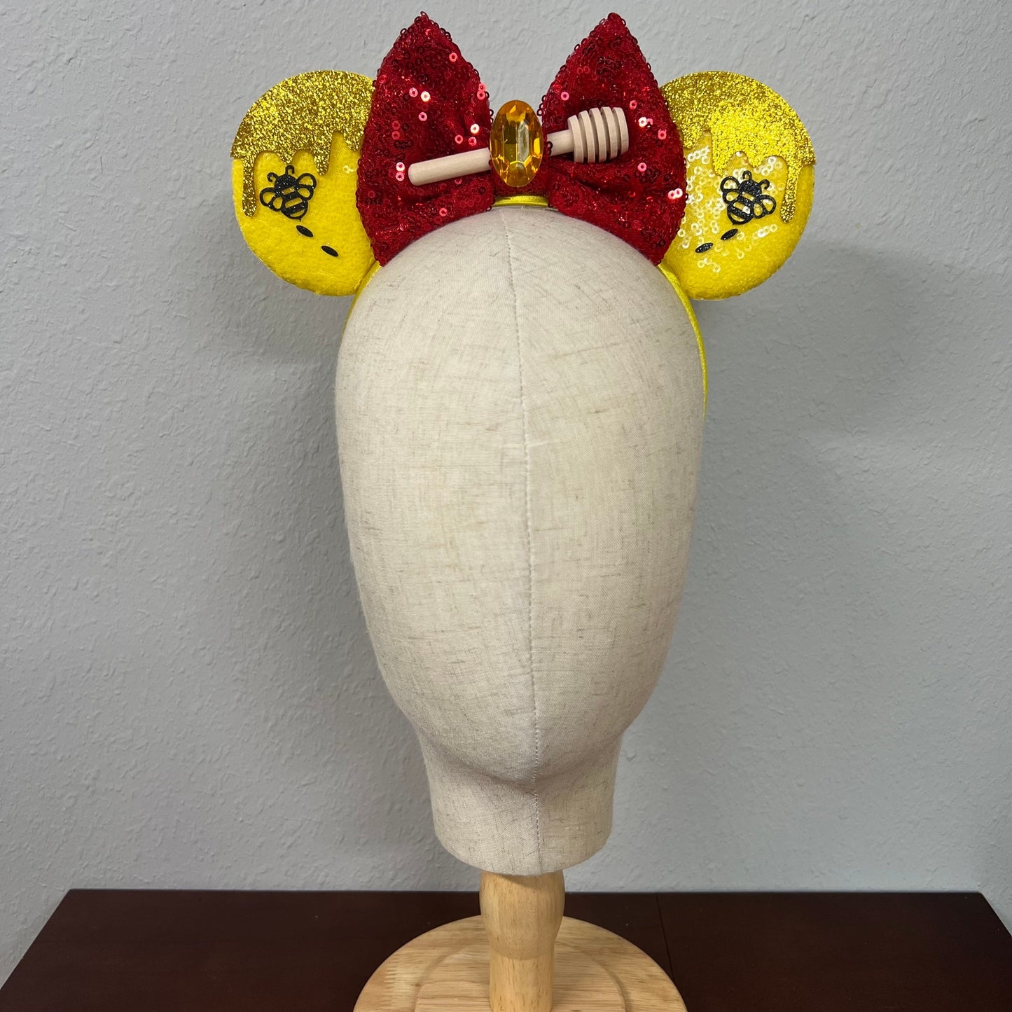 Mannequin head wearing a red and yellow bow with glittery ears on a plain background