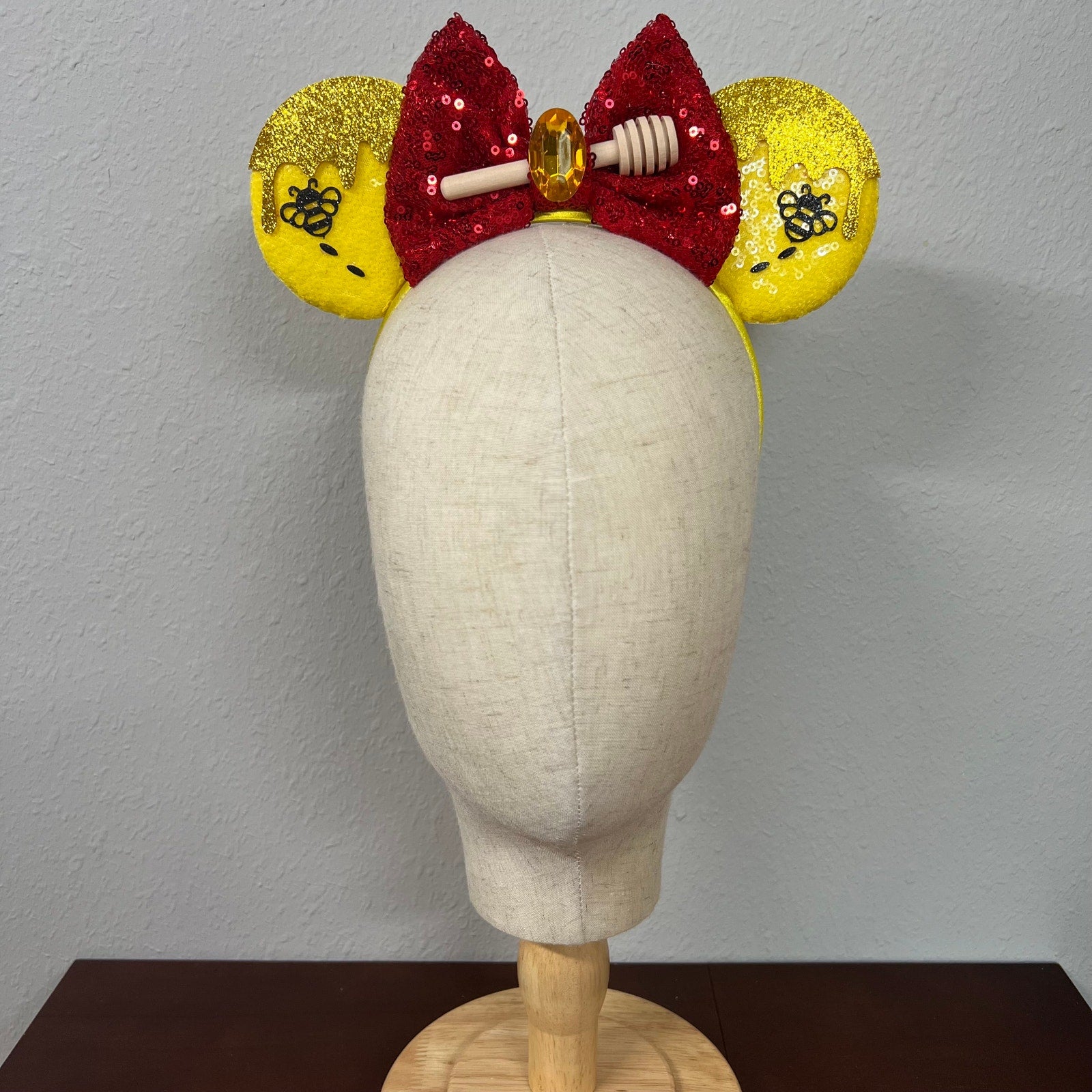 Mannequin head wearing a red and yellow bow with glittery ears on a plain background