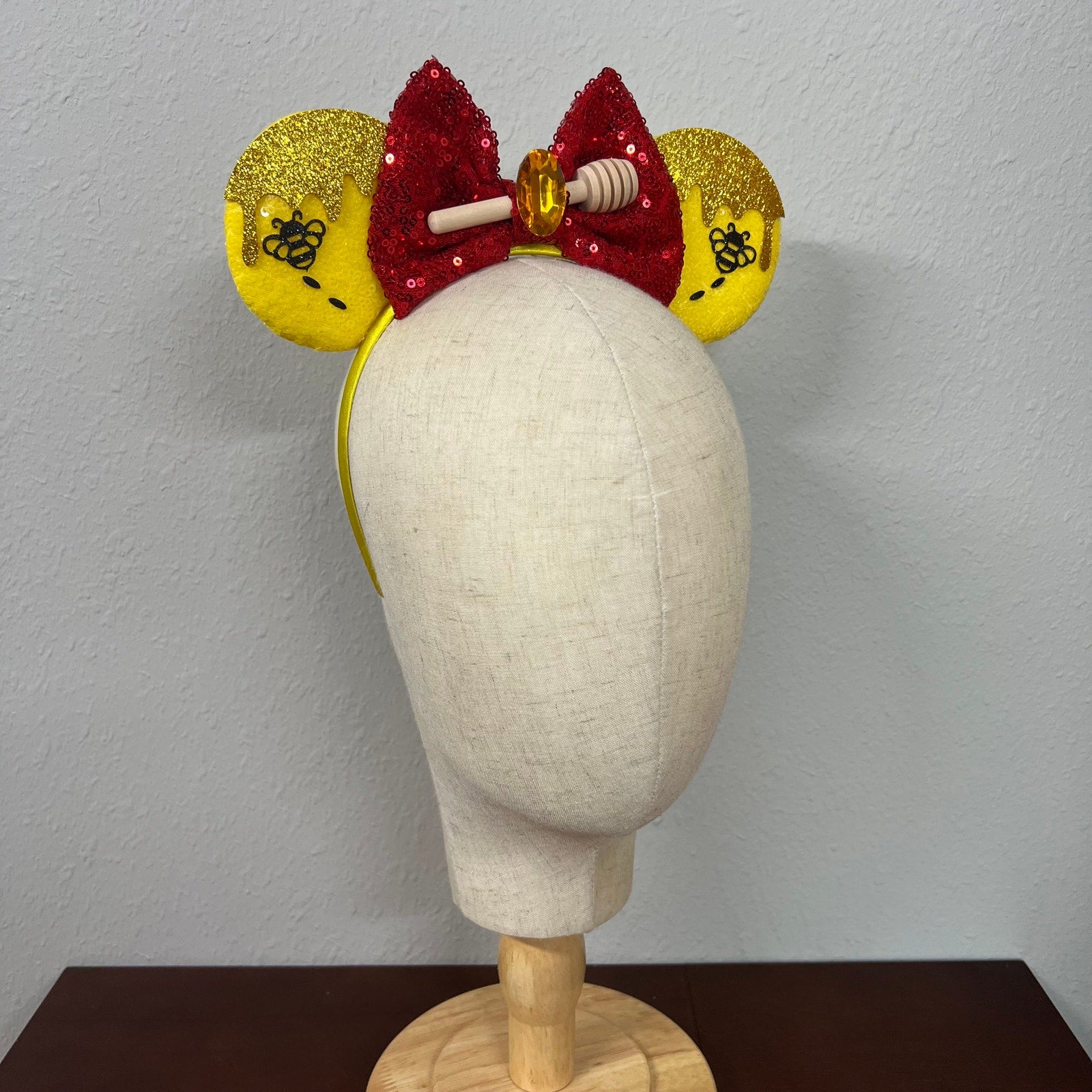 Decorative headband with yellow ears and red bow on a mannequin head against a plain background