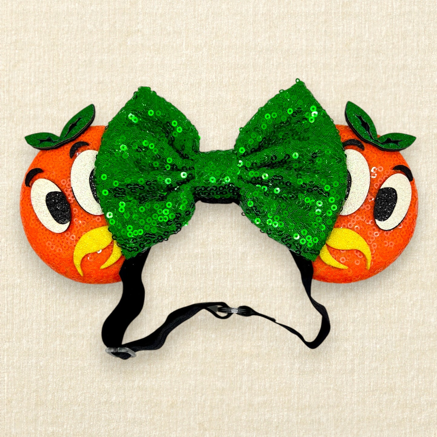 Orange mouse ears on an elastic headband with green sequin bow and glitter bird details