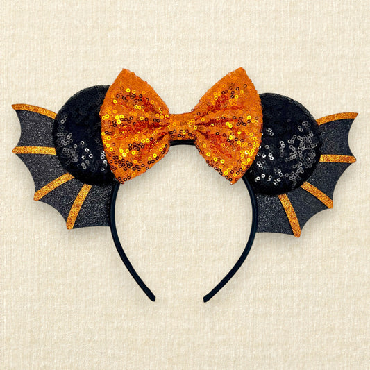 Halloween-themed headband with orange bow and black bat wings on a beige background