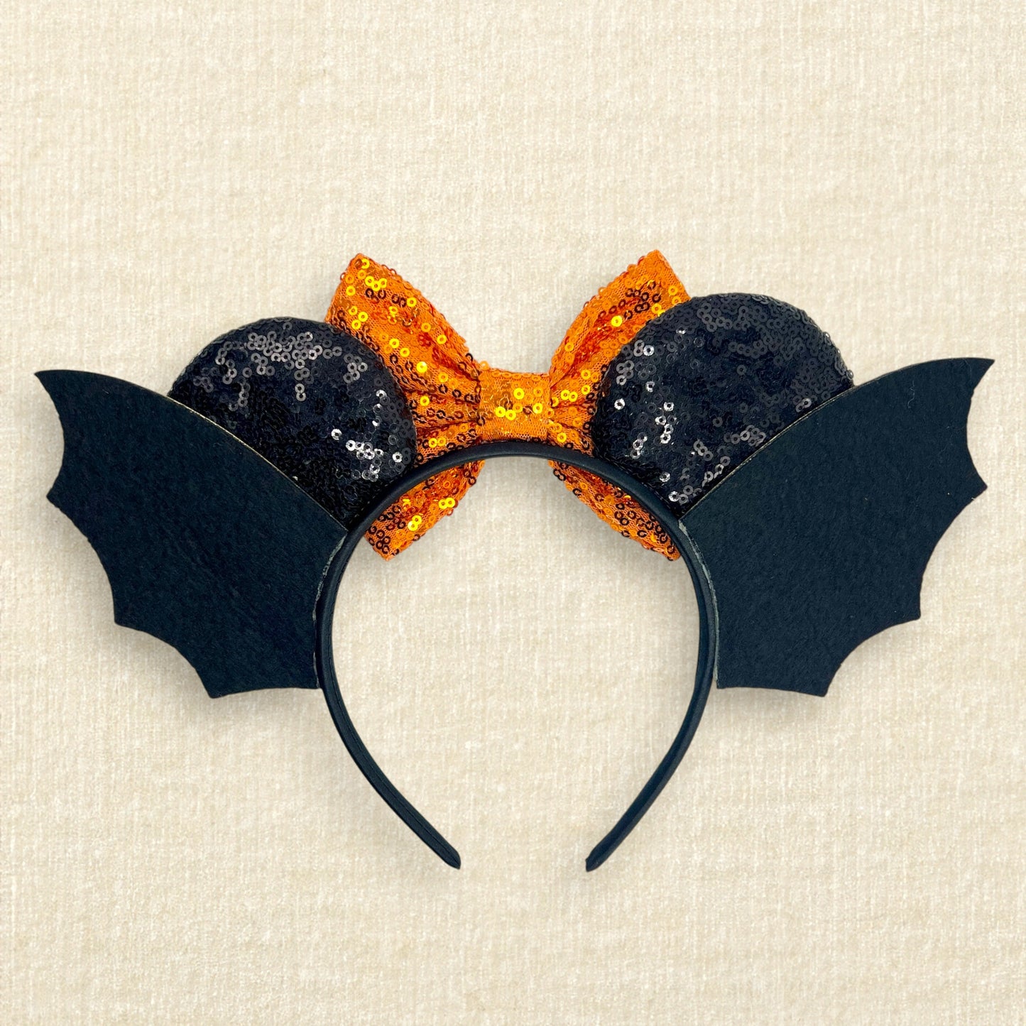 Halloween-themed headband with orange bow and black bat wings on a beige background (back view)