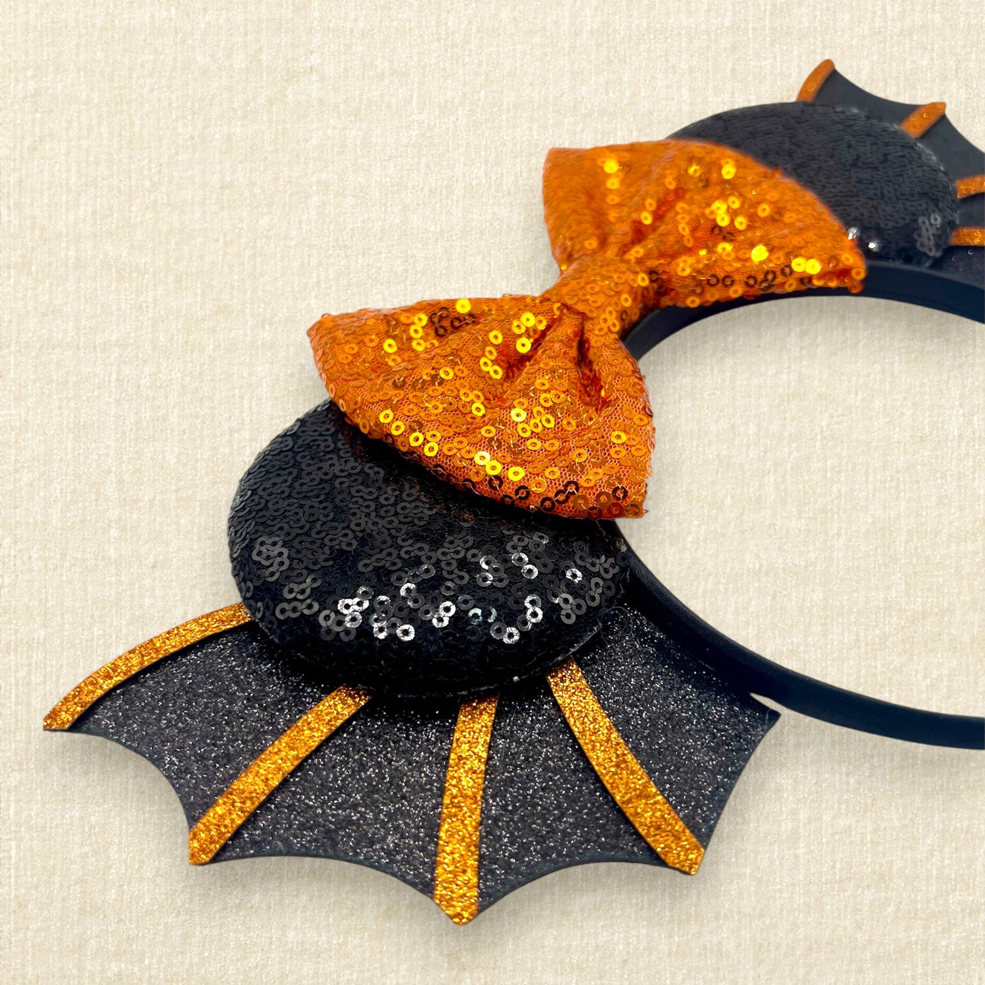 Halloween-themed headband with orange bow and black bat wings on a beige background