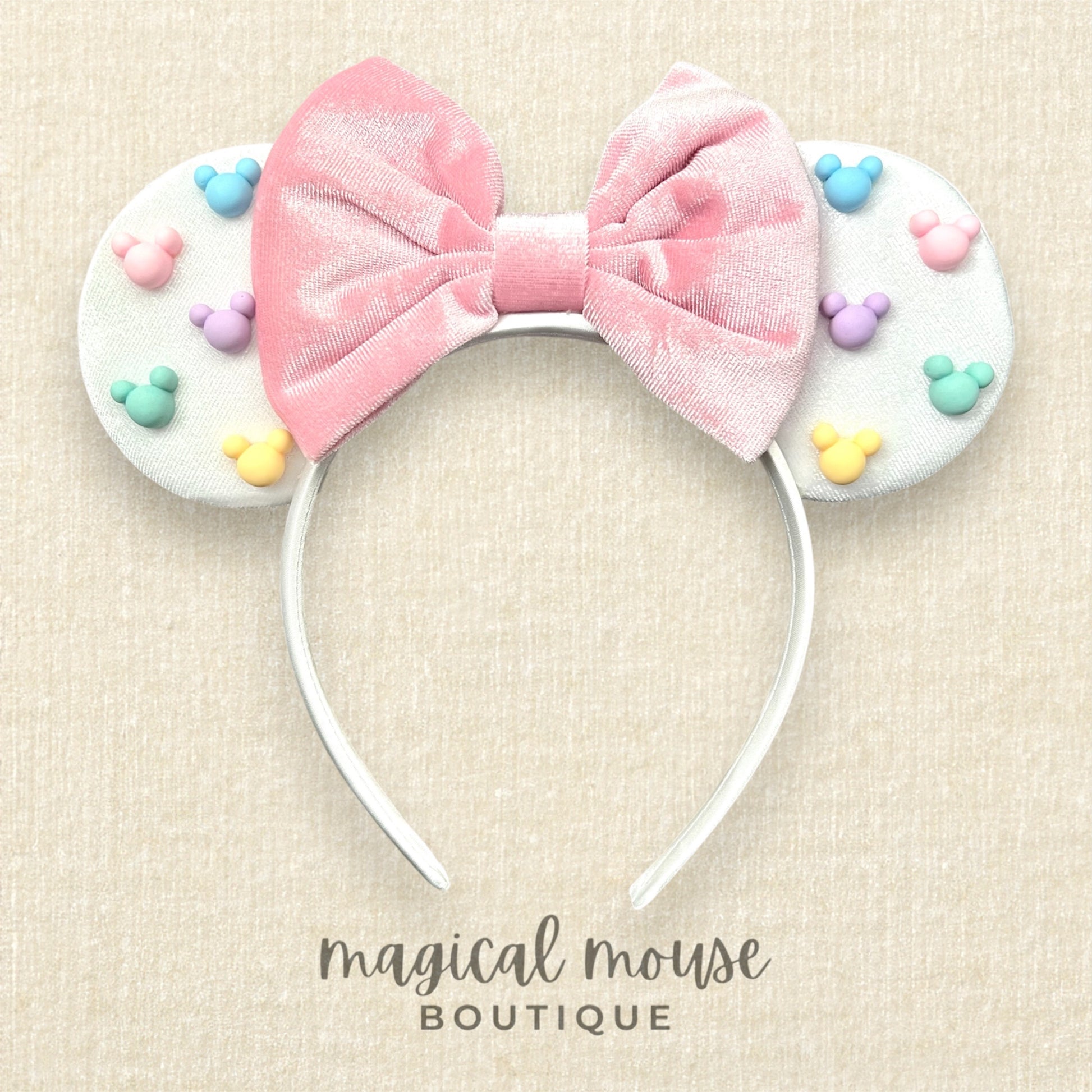 White mouse ears with a pink bow and pastel mouse-shaped pearls on a beige background, branded 'magical mouse boutique'.
