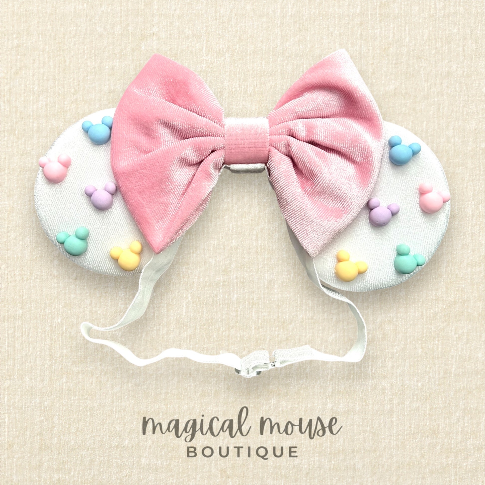 White mouse ears with pastel pink bow and pastel mouse shaped pearls on a beige background, featuring 'magical mouse boutique' branding.