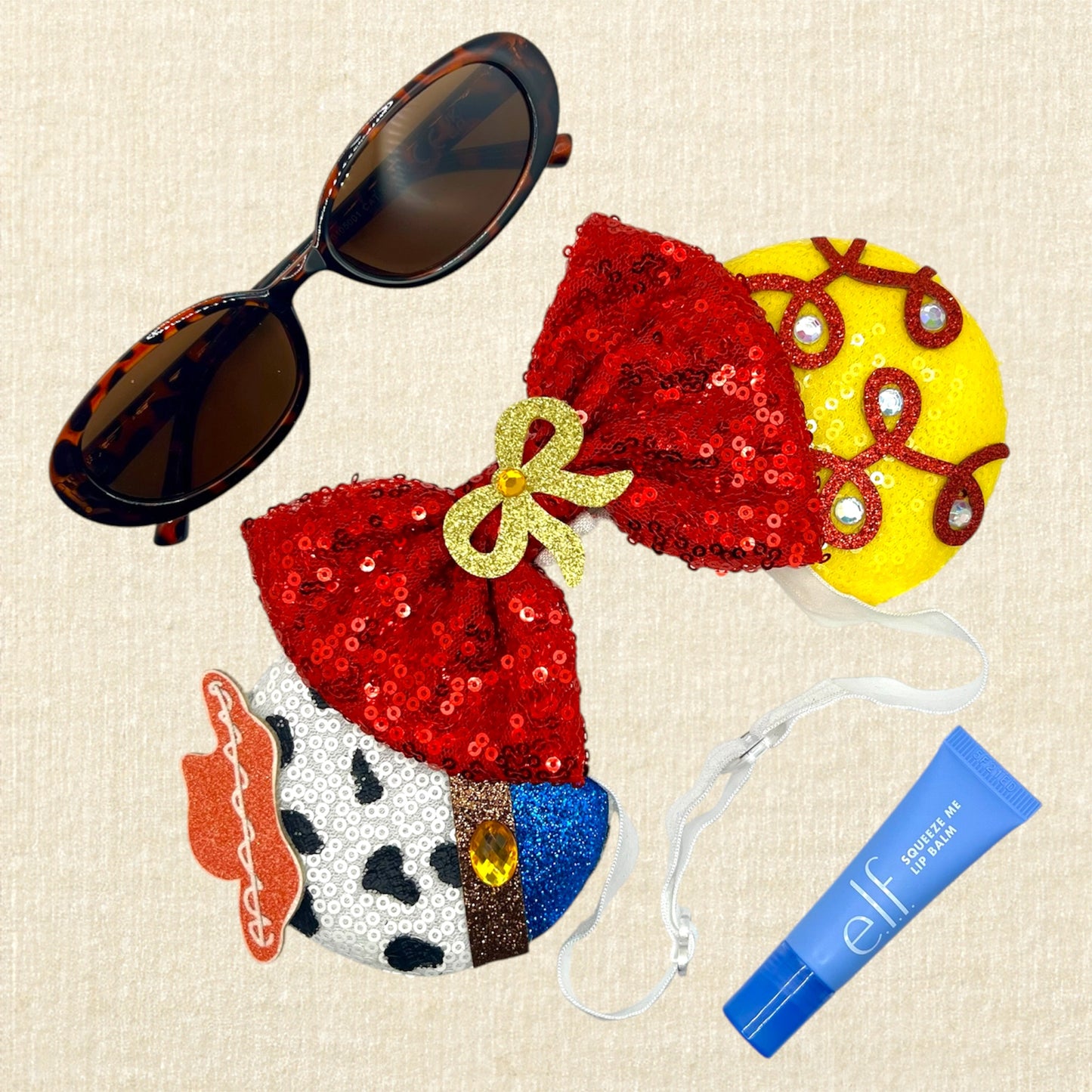 Colorful cowboy-themed mouse ears headband with glitter details, rhinestones, and red sequin bow on an elastic headband; sunglasses; blue lip balm