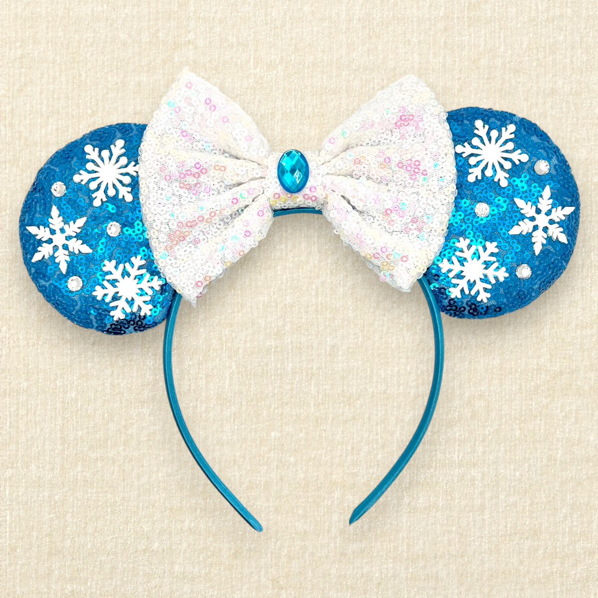 Winter-themed blue sequin mouse ears headband with white snowflakes, an iridescent white sequin bow, and blue and crystal rhinestone accents.
